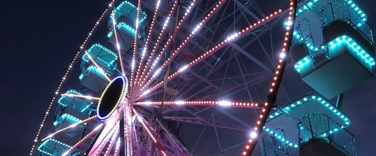 Ferris wheel lit with pink and teal lights at night